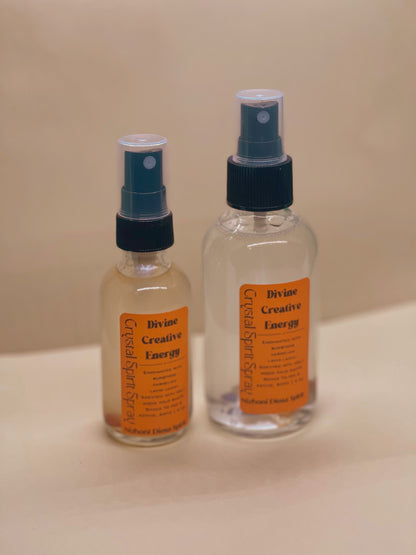 Two bottles of 'Divine Creative Energy' spray on a beige surface with a beige background.