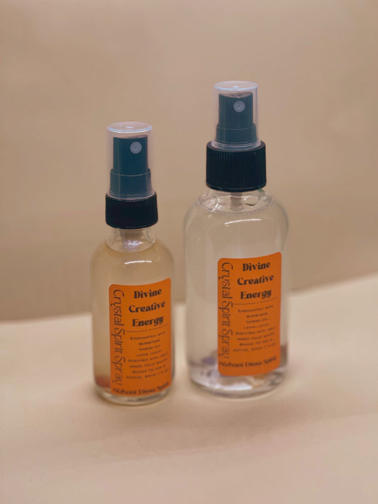 Two bottles of 'Divine Creative Energy' spray on a beige surface with a beige background.